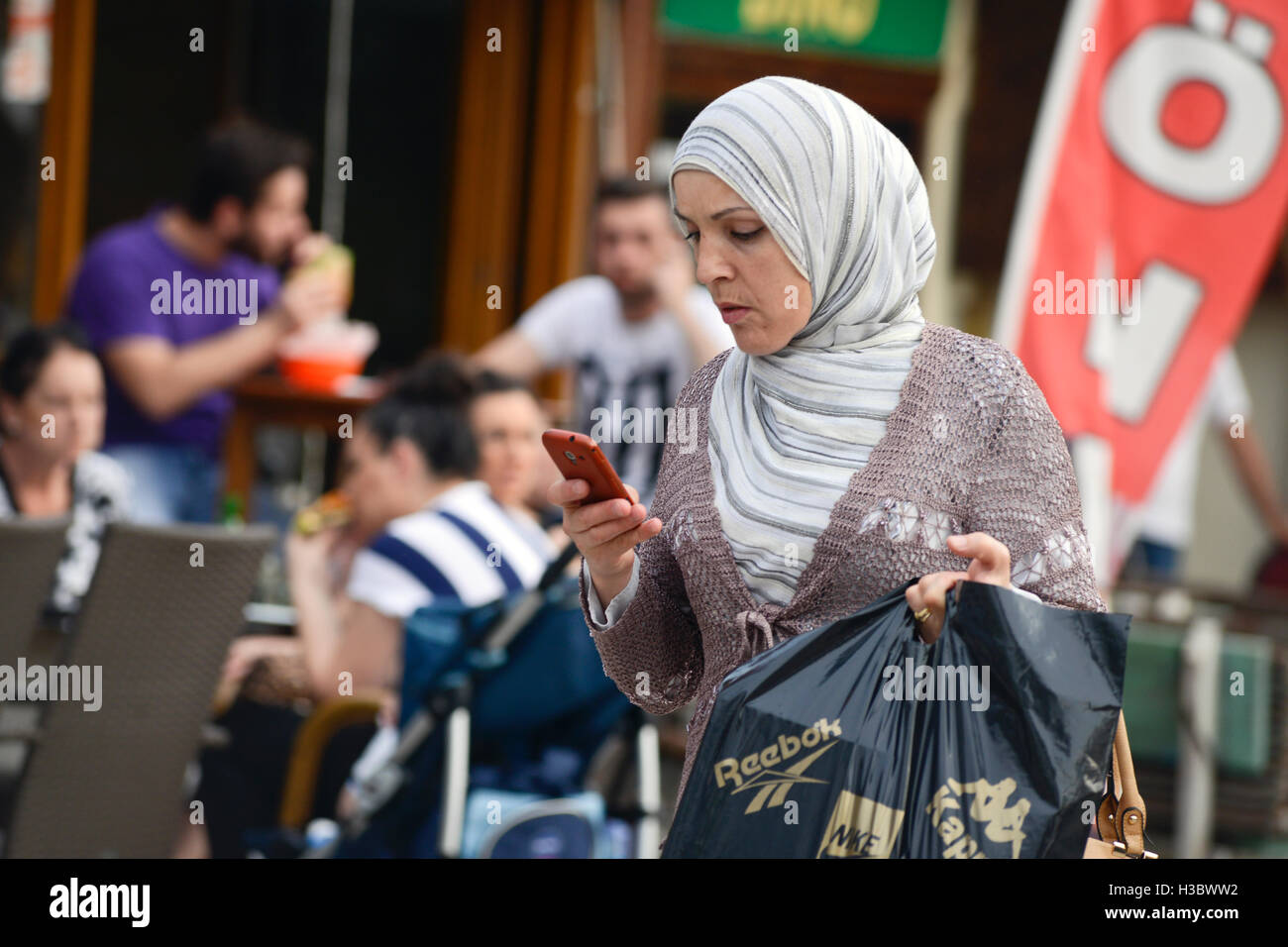 Donna musulmana camminare per la strada a Sarajevo Città Vecchia, Bosnia e Erzegovina, con le borse della spesa e un telefono cellulare Foto Stock