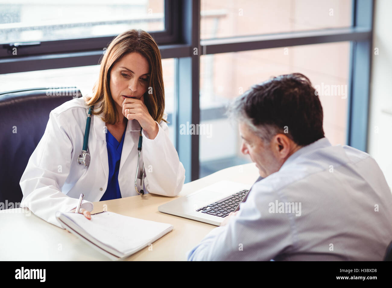 Medico donna seduta alla sua scrivania parlando al paziente Foto Stock