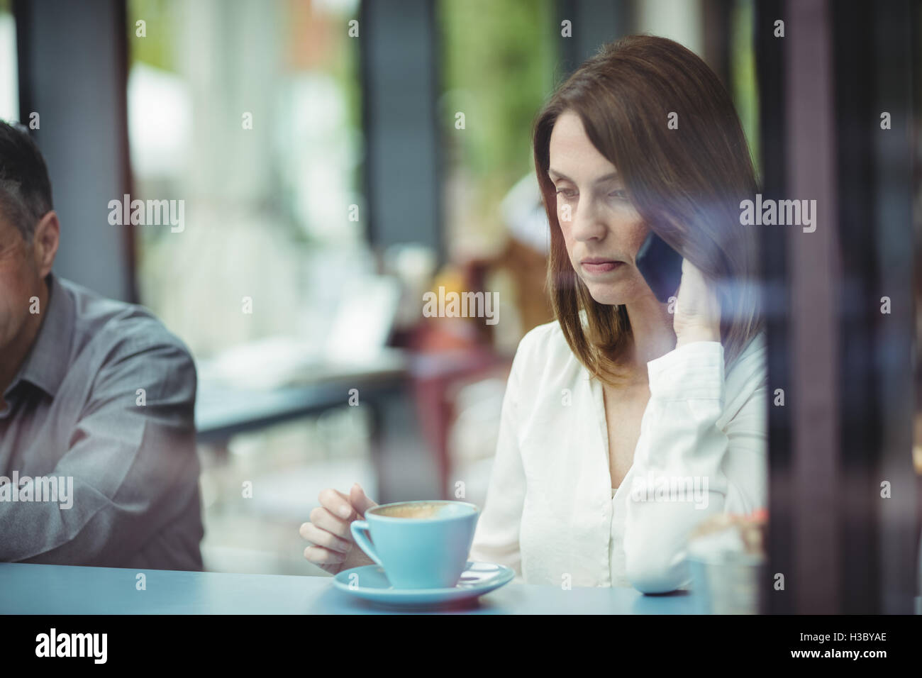 Donna che mantiene tazza di caffè e parlando al telefono cellulare Foto Stock