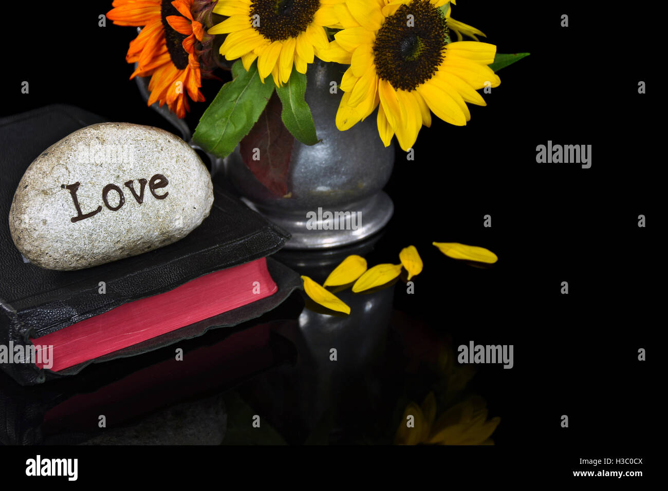 La parola amore scolpito in pietra sulla Sacra Bibbia con bouquet di semi di girasole in peltro brocca Foto Stock