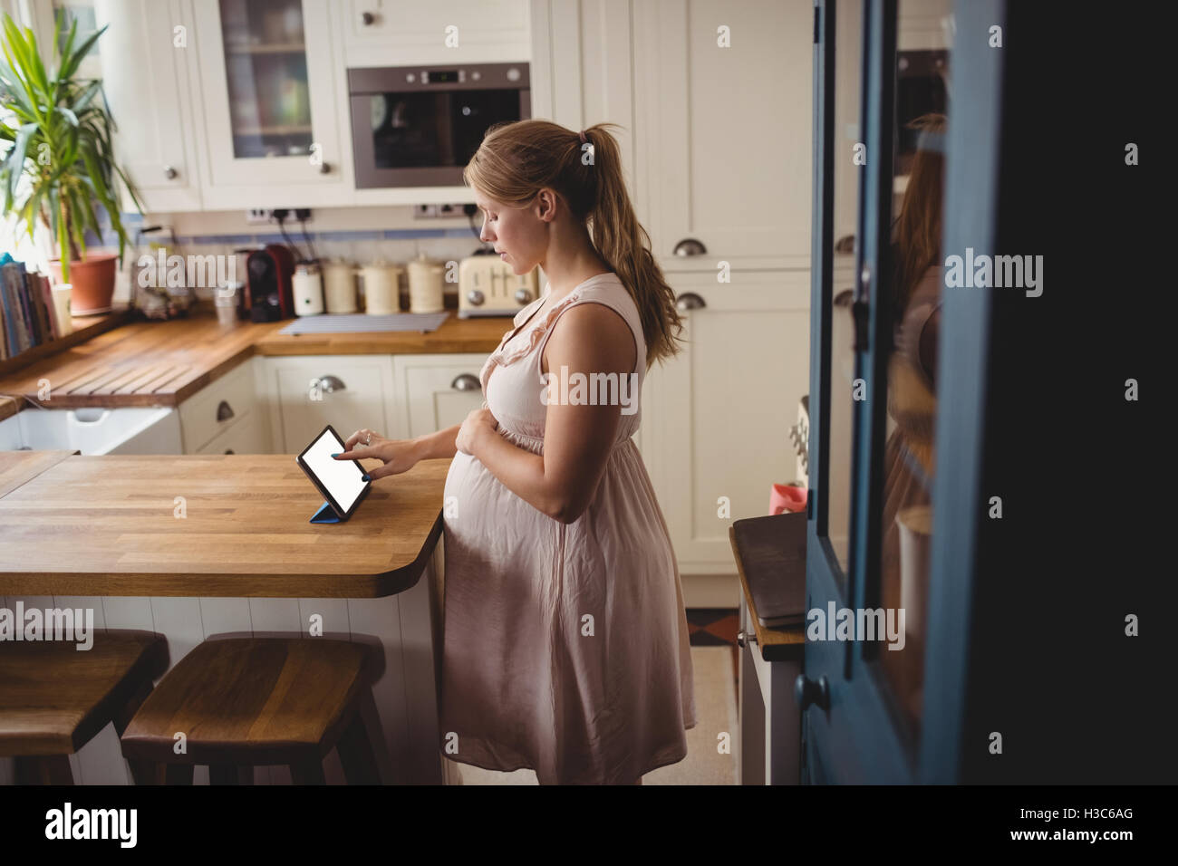Donna incinta con tavoletta digitale in cucina Foto Stock