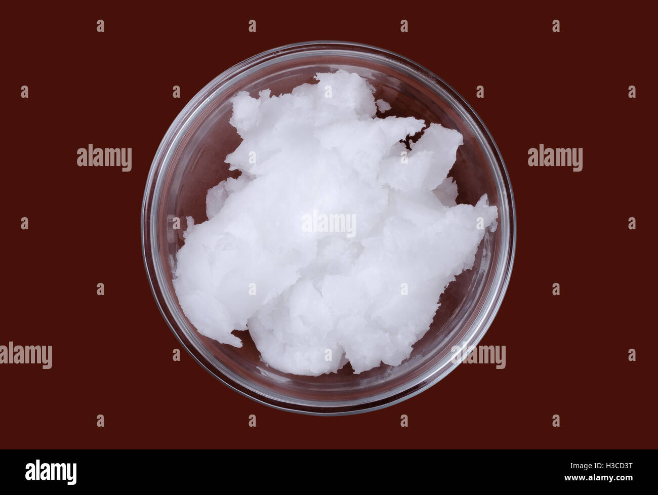 Olio di noce di cocco in recipiente di vetro su sfondo marrone. Anche olio di copra, un olio commestibile, estratta dal kernel di carni di noci di cocco mature. Foto Stock