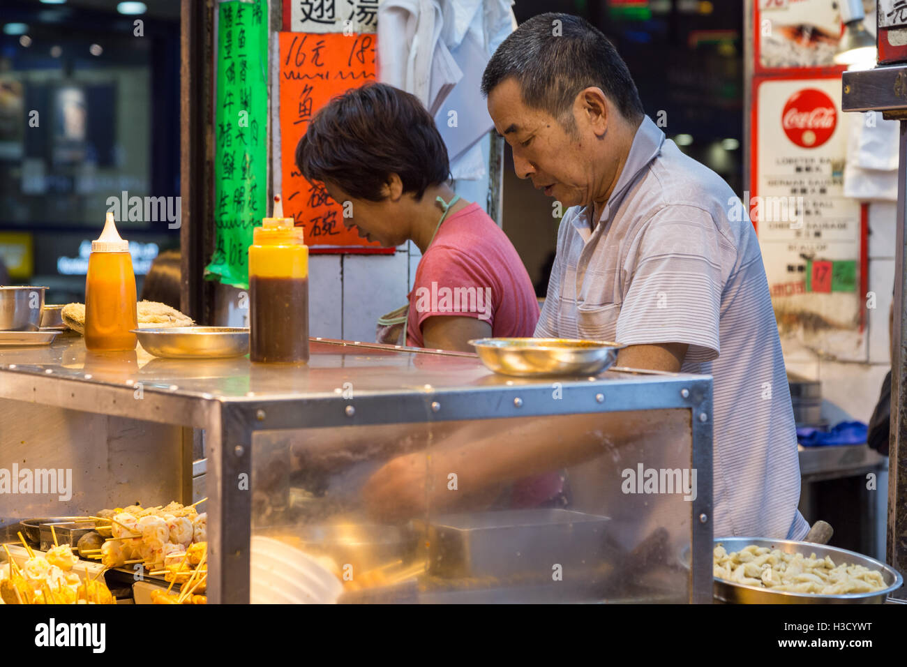 Un uomo e una donna preparare spuntini in un cibo di strada stallo a angolo di Prat e Hart Aves in Tsim Sha Tsui, Kowloon, Hong Kong. Foto Stock