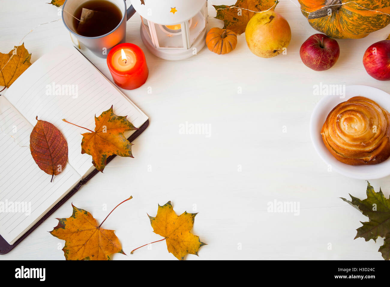 Decorazioni in autunno con le foglie, notebook, candela,,zucca lanterna, tazza di tè, cannella bun e la frutta in bianco sullo sfondo di legno Foto Stock