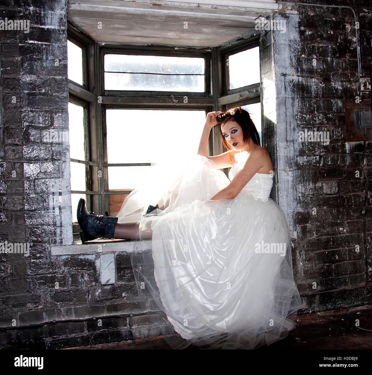 Giovane donna in posa di edificio abbandonato finestra in abito da sposa e  stivali neri Foto stock - Alamy