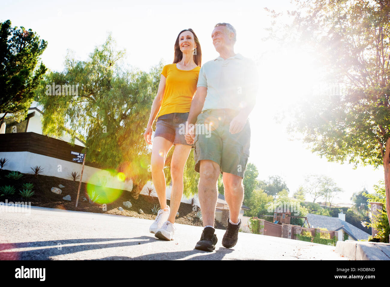 Coppia senior che indossano pantaloncini a piedi lungo una strada del sole. Foto Stock