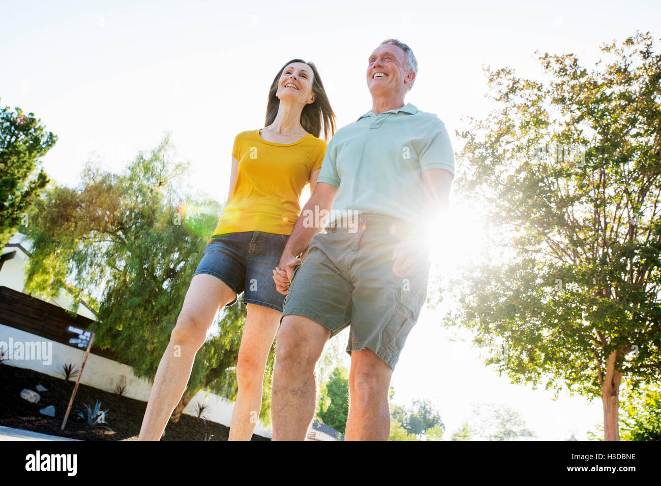 Coppia senior che indossano pantaloncini a piedi lungo una strada del sole. Foto Stock