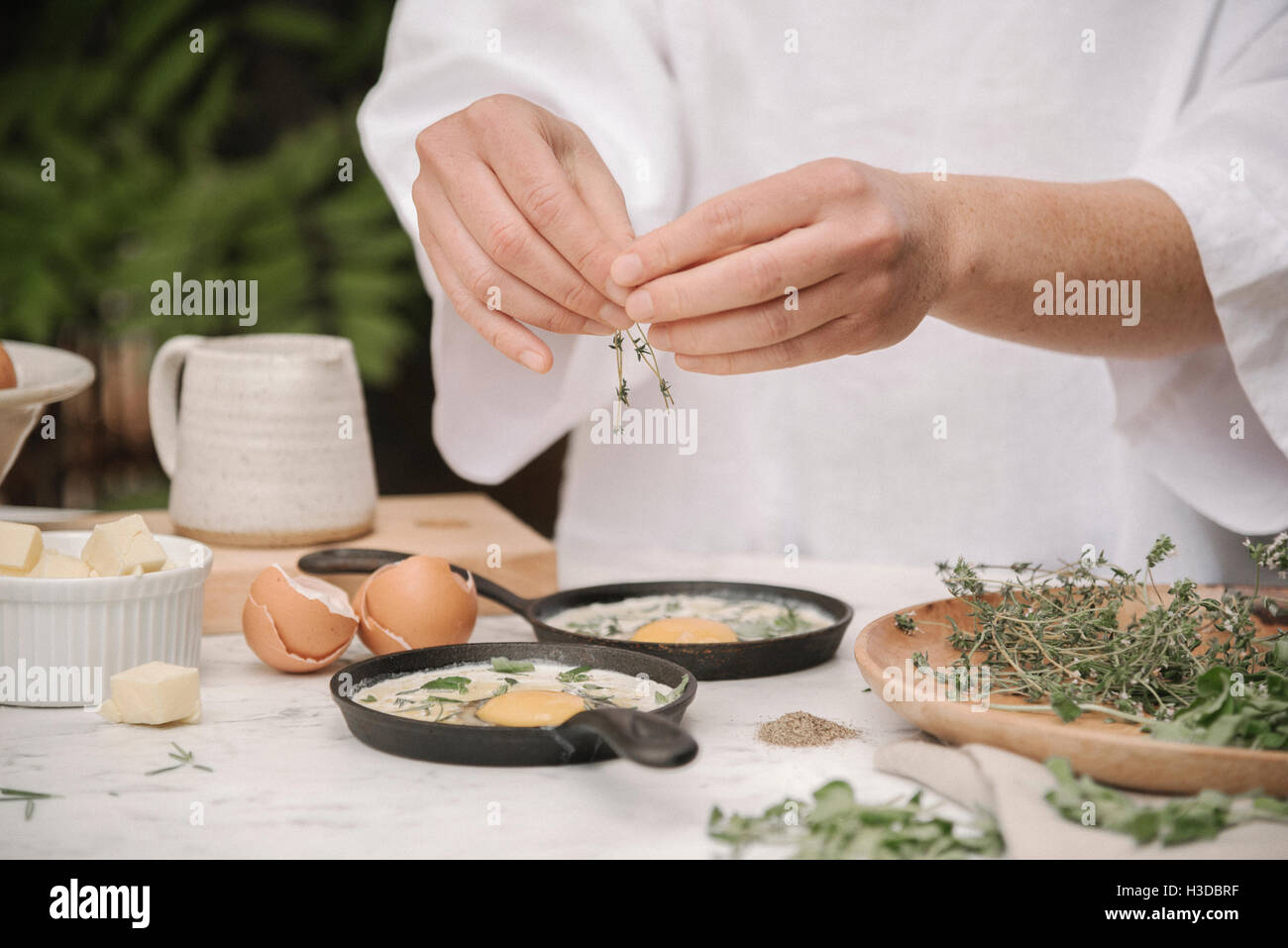 Una donna aggiungere erbe per le uova incrinate in due piccole teglie. Foto Stock