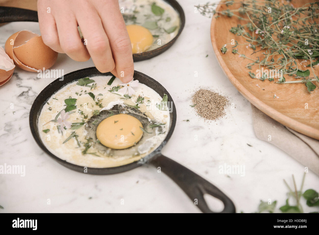 Una donna spruzzando le erbe in un uovo fresco in una padella. Foto Stock