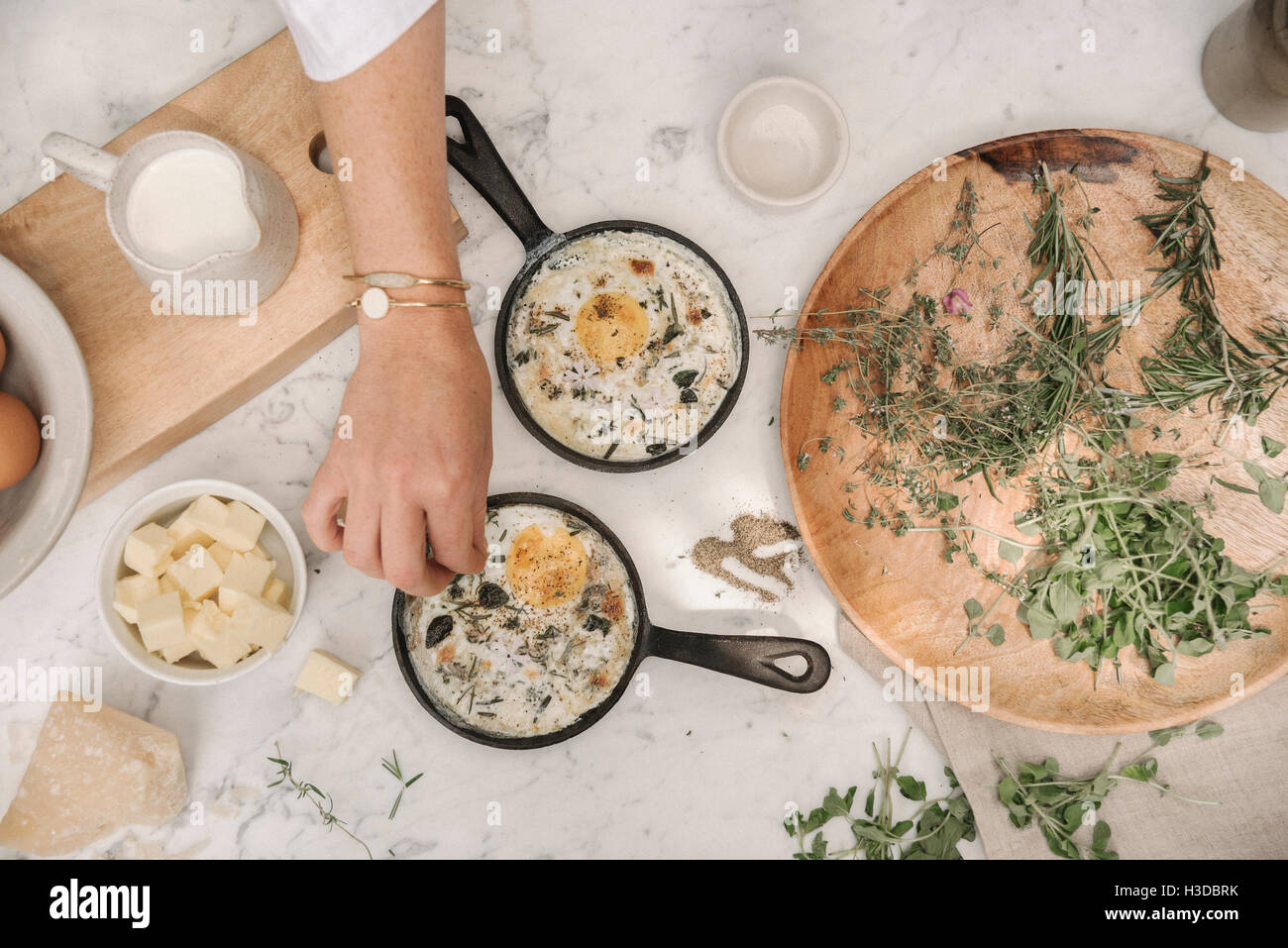 Una donna spruzzando le erbe in un uovo fresco in una padella. Foto Stock