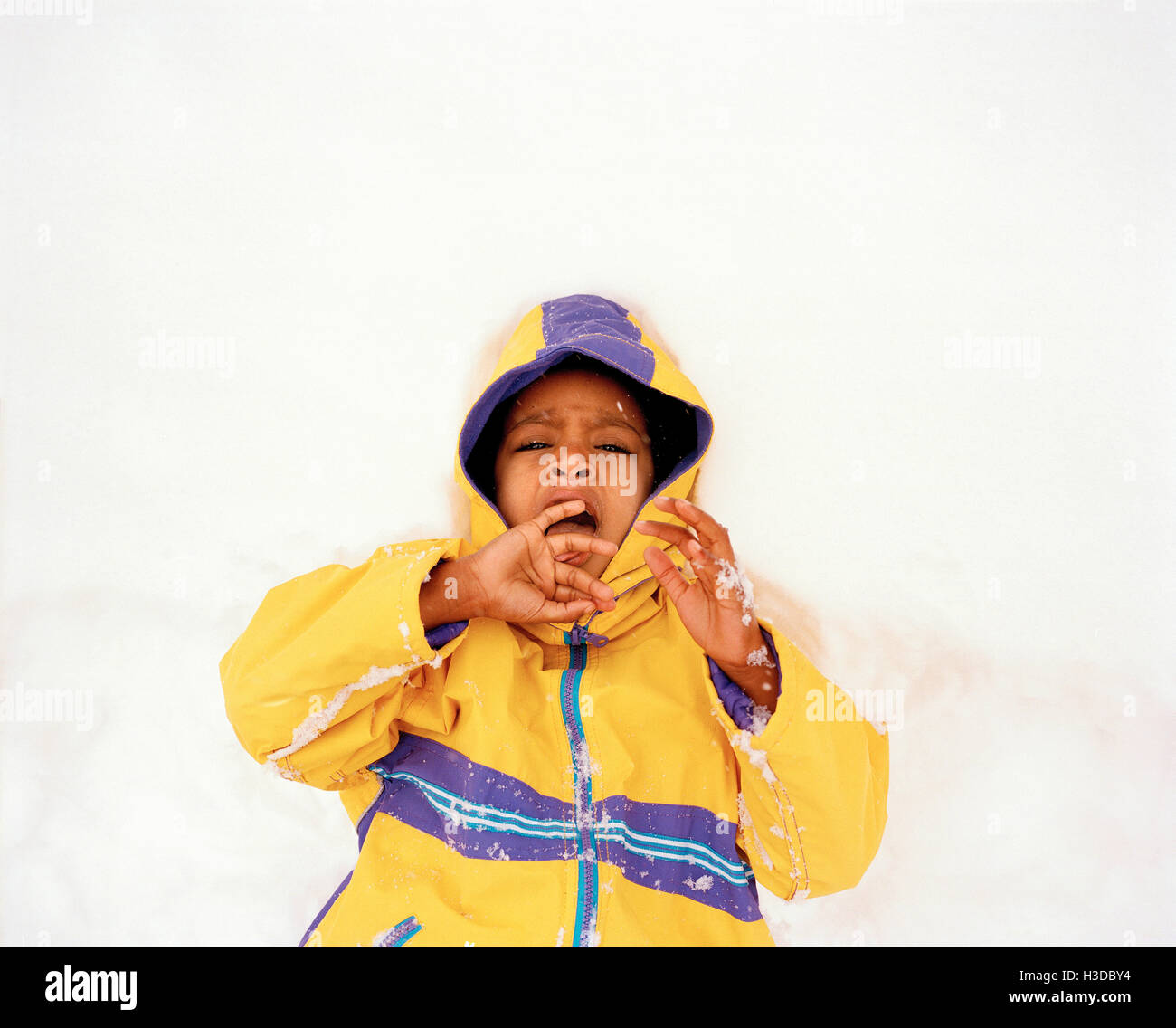 Ragazzo che indossa un cappotto giallo giacente nella neve. Foto Stock