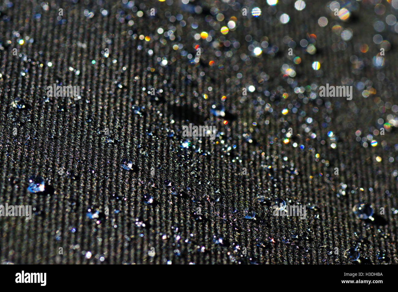 Gocce di acqua su un nero materiale impregnato nella luce del sole. Foto Stock