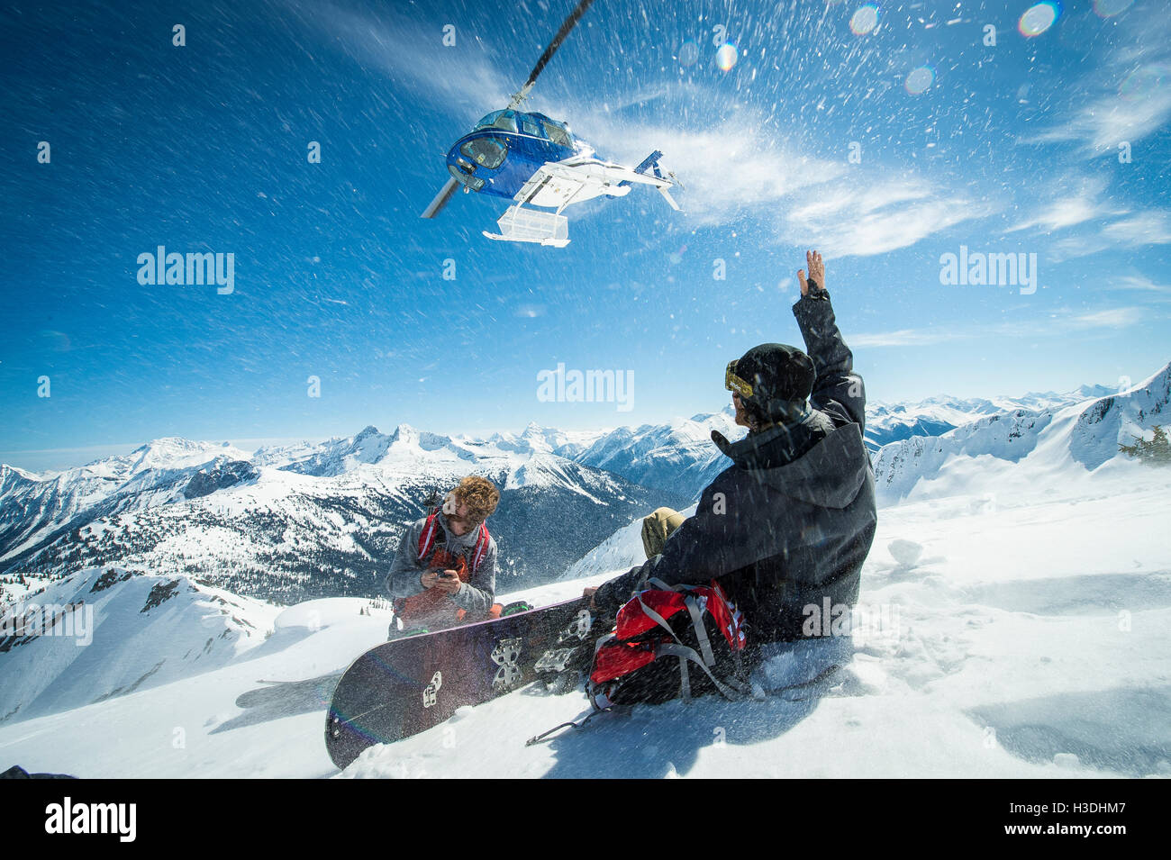 Gli appassionati di snowboard guardando un heli decollare dopo essere stata scaricata su un picco remoto nel backcountry Foto Stock