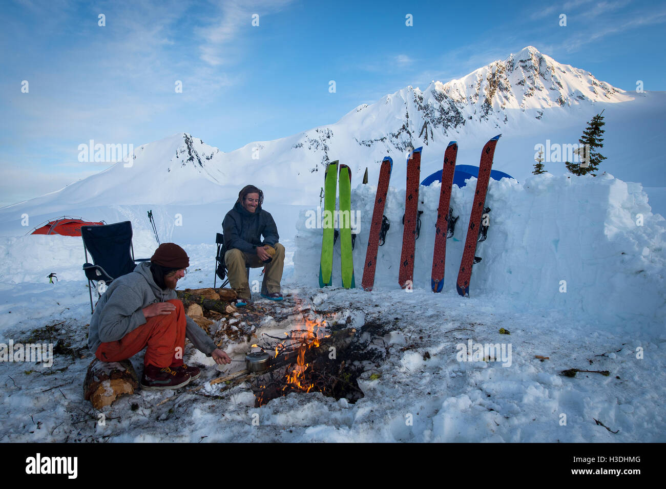 Gli appassionati di snowboard appendere fuori attorno a un fuoco durante il tramonto al campo base Foto Stock