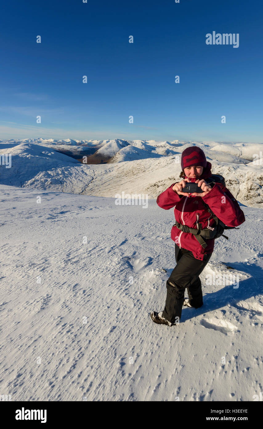 Femmina walker hill tenendo il telefono cellulare fotografie dal vertice di Ben Challum (un Munro), vicino a Crianlarich Scozia Foto Stock