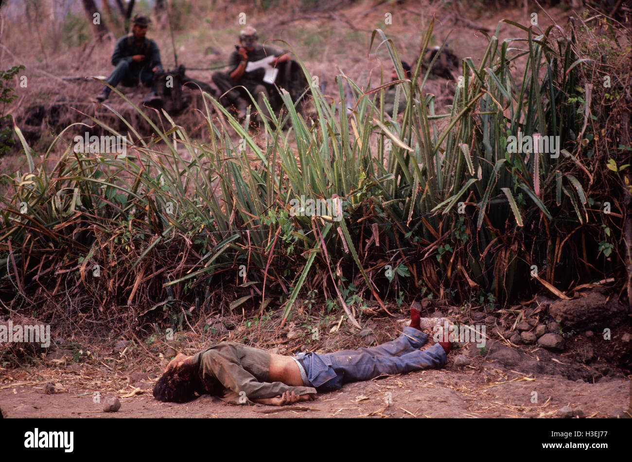 NORTHERN MORAZAN provincia, EL SALVADOR, Marzo 1984: un morto FMLN guerrilla si trova dove è caduto dopo un agguato di guerriglia della brigata Cuscatlan. I soldati attendere helecopter evacuazione. Foto Stock