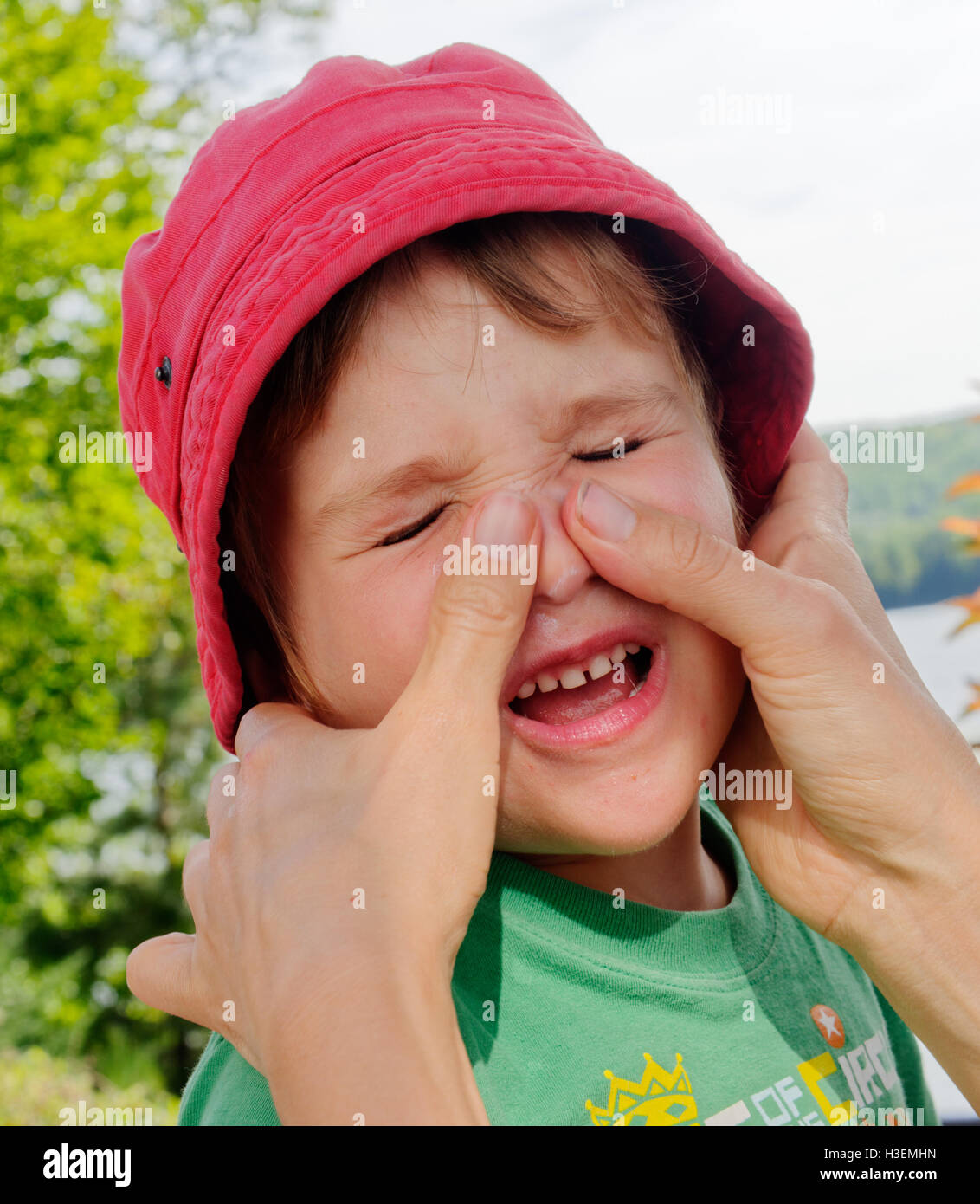 Un giovane ragazzo (4 anni) a malincuore avente crema solare messo sul suo volto da sua mamma Foto Stock