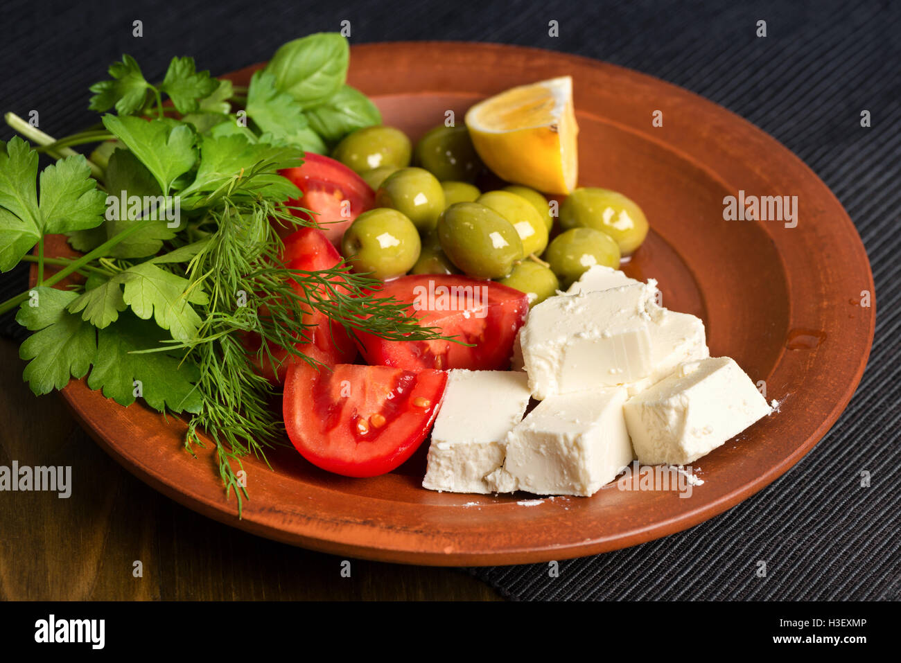 Il formaggio feta, pomodori, olive ed erbe in una lastra di argilla - Greco il pranzo Foto Stock