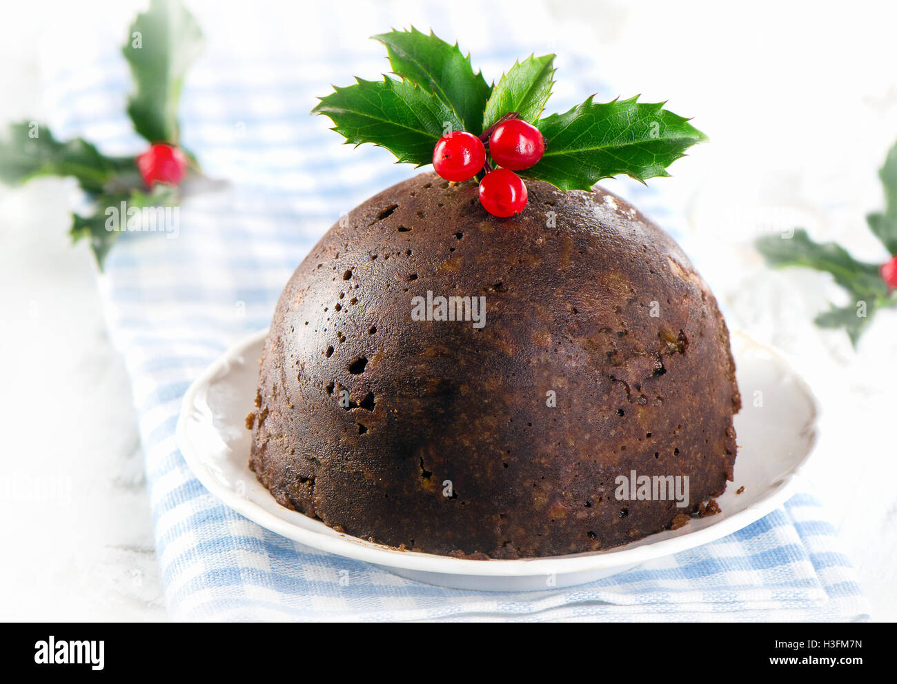 Pudding natalizio con holly su una piastra bianca. Messa a fuoco selettiva Foto Stock