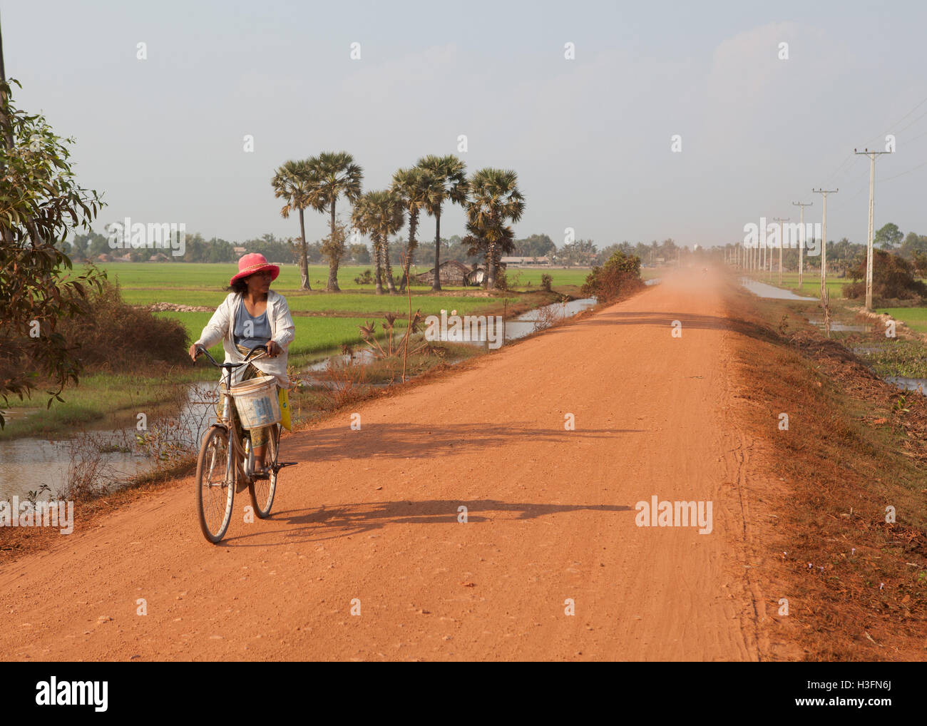 Donna in bicicletta giù per una strada polverosa vicino a Siem Reap,Cambogia Foto Stock