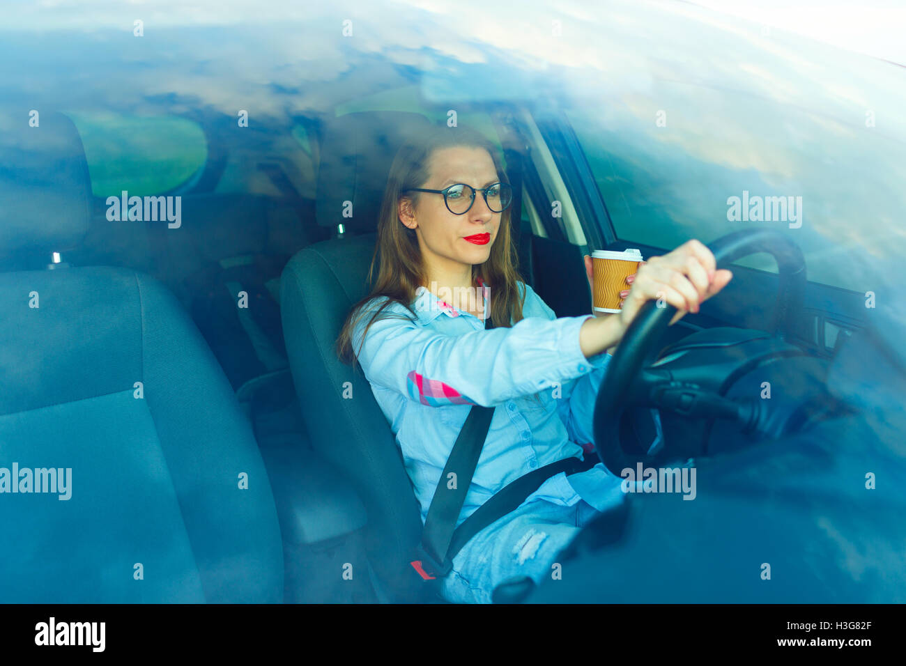 Bella giovane donna con il caffè per andare alla guida la sua automobile Foto Stock