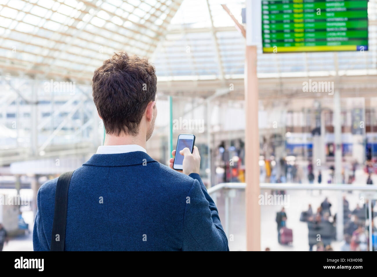 Traveler inviando un messaggio di testo sullo smartphone con treno orario in background Foto Stock