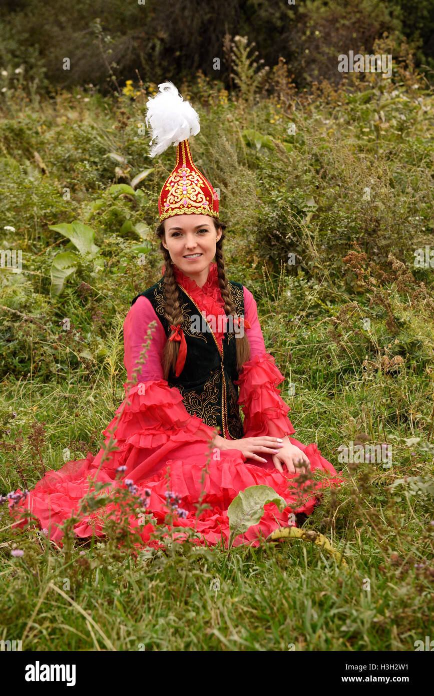 Giovane donna nel tradizionale abito kazako seduto in un campo al villaggio degli Unni Kazakistan Foto Stock
