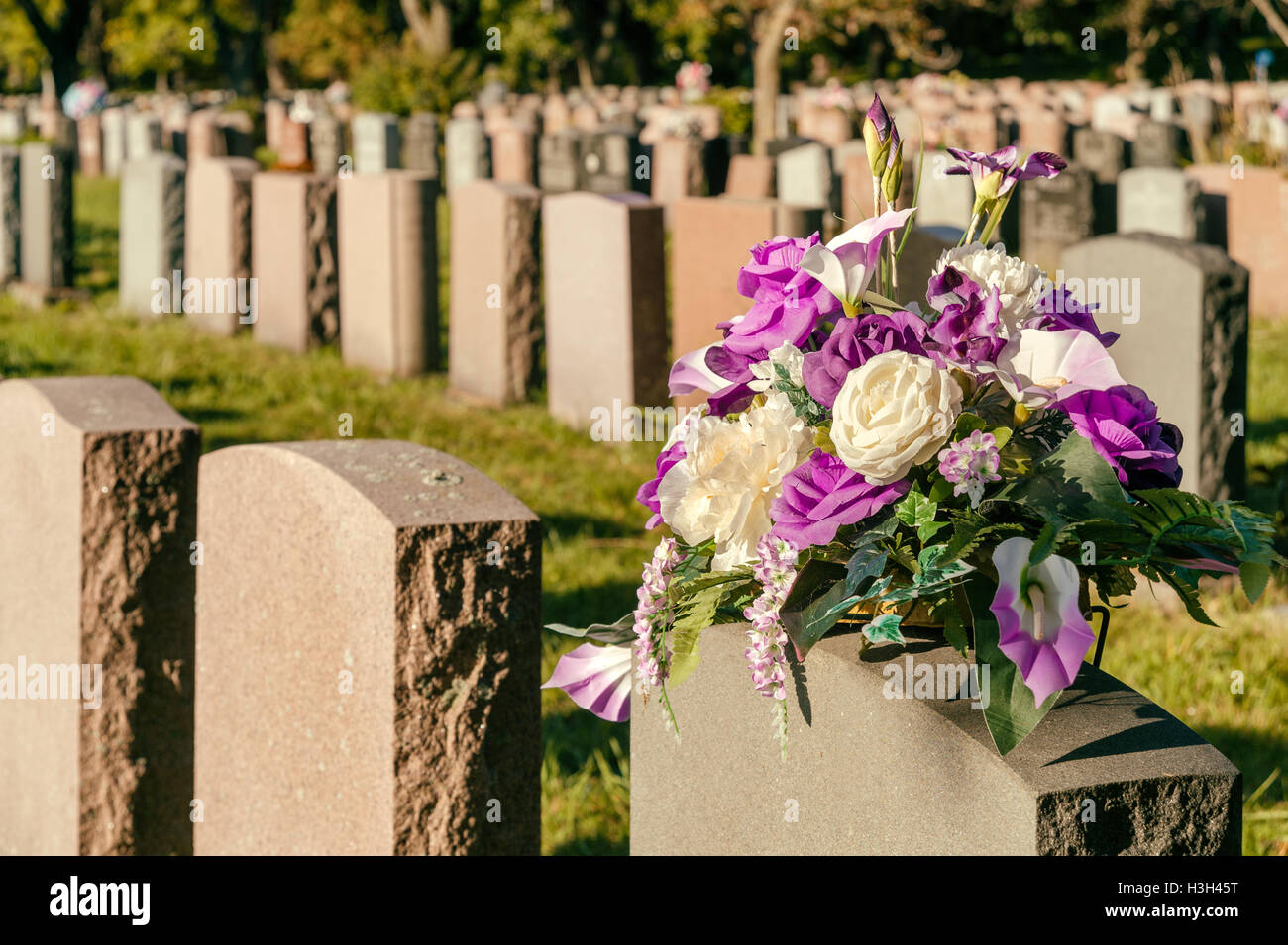 Fiori in un cimitero con lapidi in background al tramonto Foto Stock