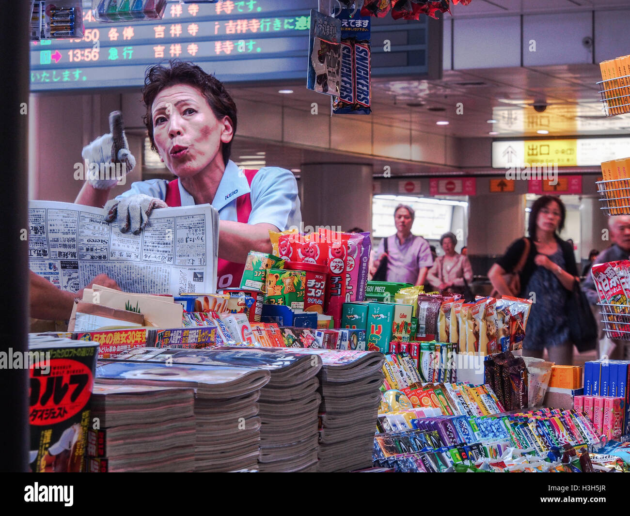 Una donna giapponese con un giornale puntando il dito, un lavoratore presso un punto di vendita al dettaglio in stallo in Shibuya stazione ferroviaria, Tokyo Giappone Foto Stock