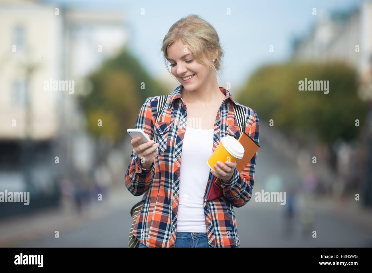 Ritratto di attraente ragazza studente contro street, guardando il telefono Foto Stock