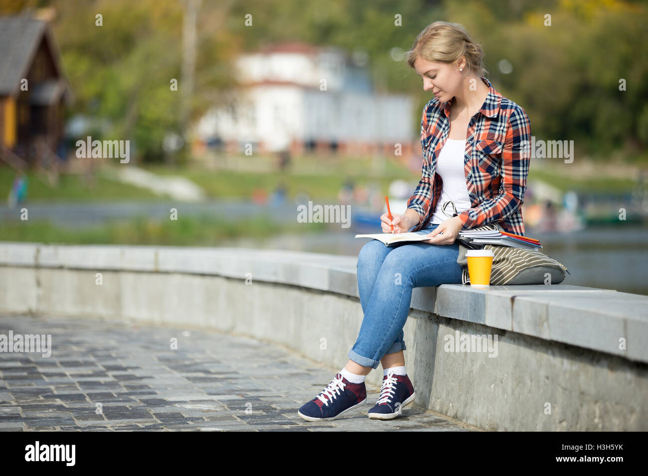 Ritratto di un attraente studente ragazza seduta a ponte la scrittura Foto Stock