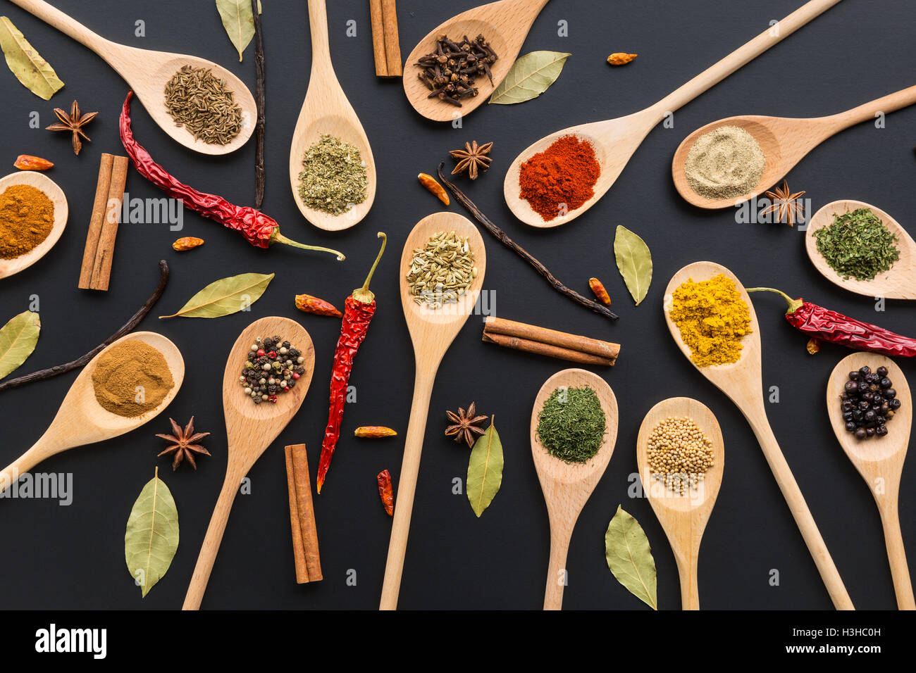 Varie spezie in cucchiai di legno su sfondo nero. Vista dall'alto. Foto Stock