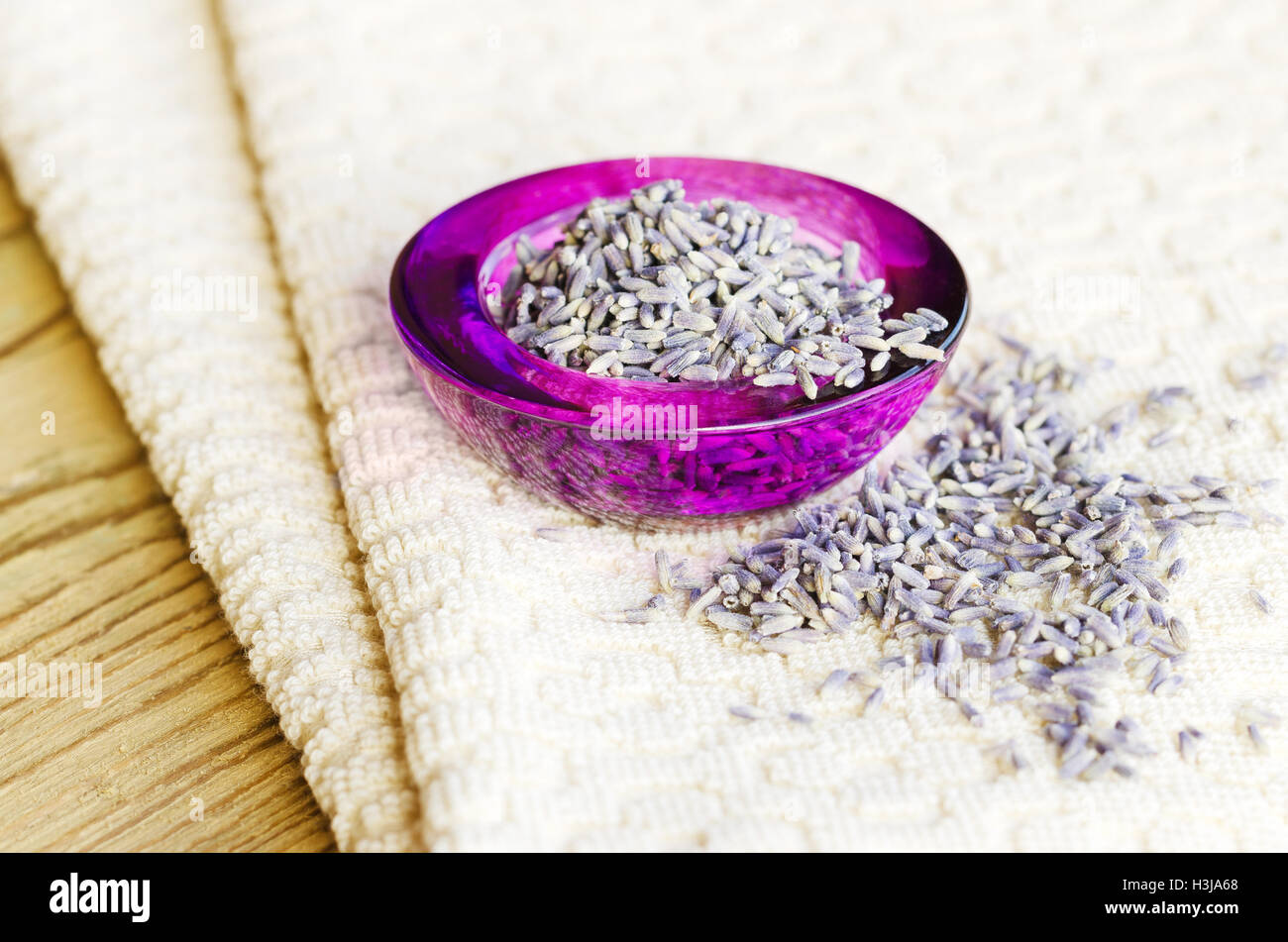 Secchi fiori di lavanda in viola ciotola di vetro sul tessuto e legno. Lavandula angustifolia con un pallido fiori viola. Erbe culinarie. Foto Stock