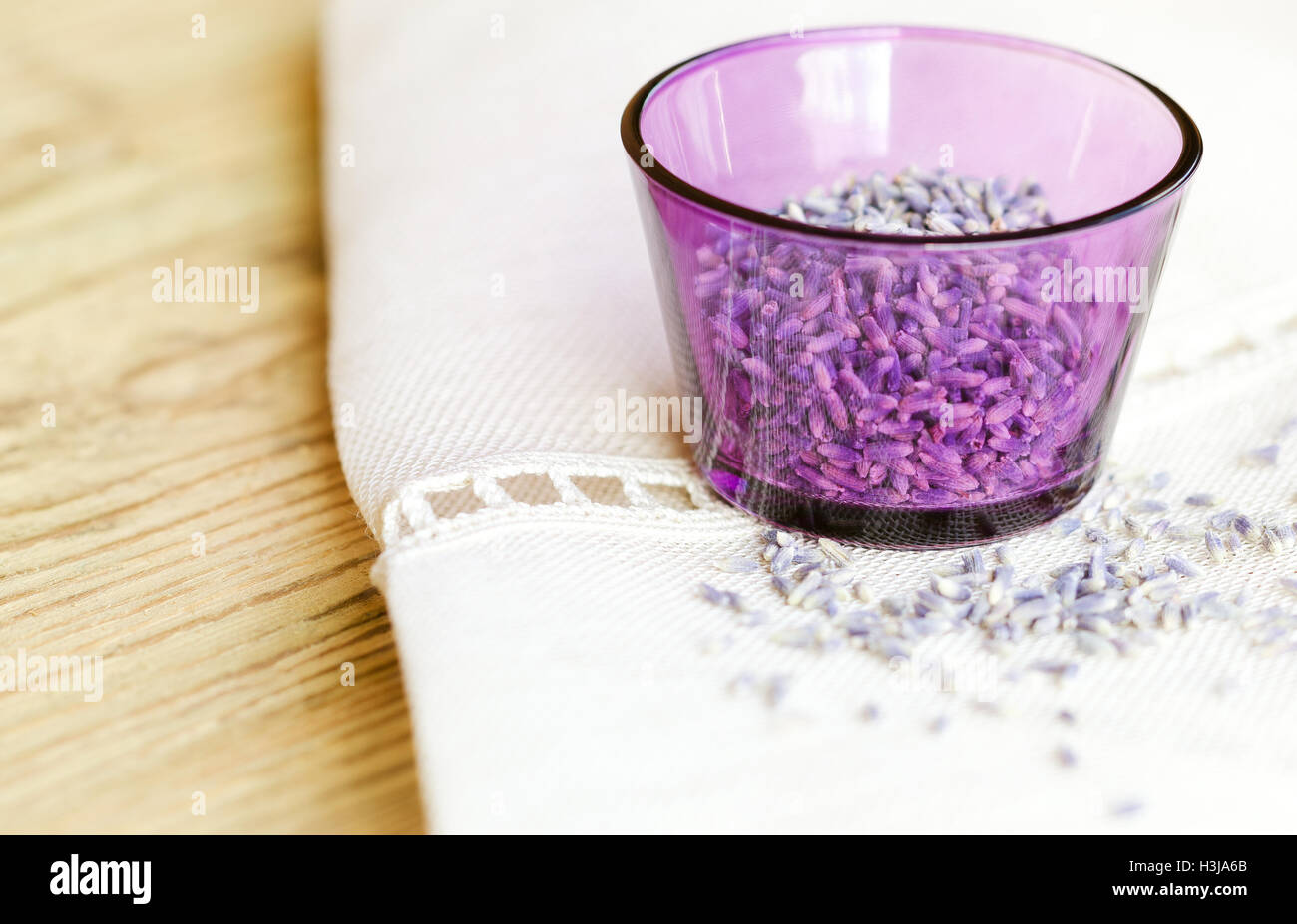 Secchi fiori di lavanda in un vetro viola sul tessuto e legno. Lavandula angustifolia con un pallido fiori viola. Erbe culinarie. Foto Stock