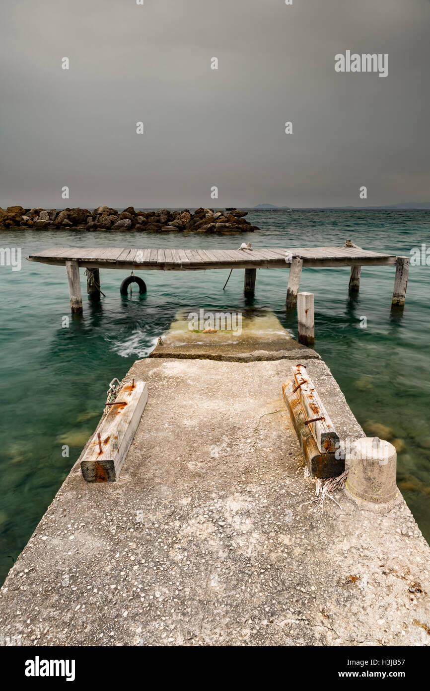 Un danneggiato e pericoloso jetty collassa in mare in Grecia come una tempesta di cloud si brucia in. Foto Stock