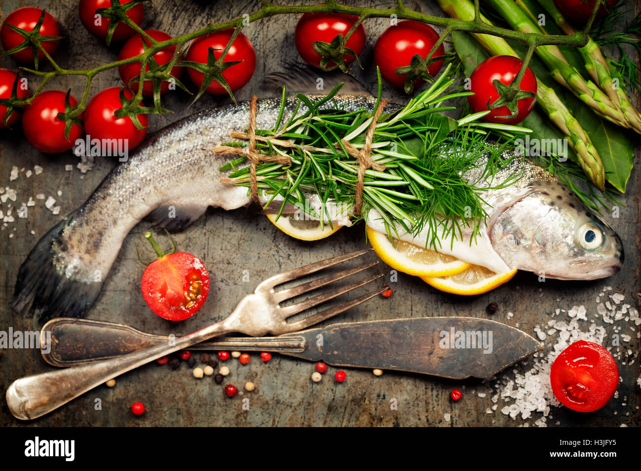 Materie della trota arcobaleno con limone, erbe aromatiche e spezie su sfondo rustico Foto Stock