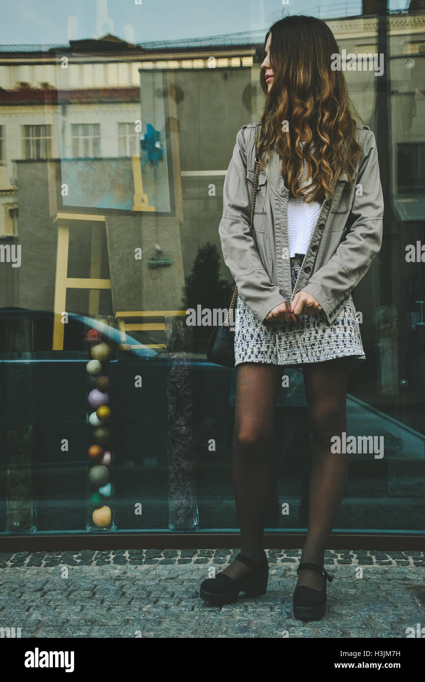 Elegante ragazza in gonna in piedi vicino al negozio di vetro di finestra sulla strada di città Foto Stock