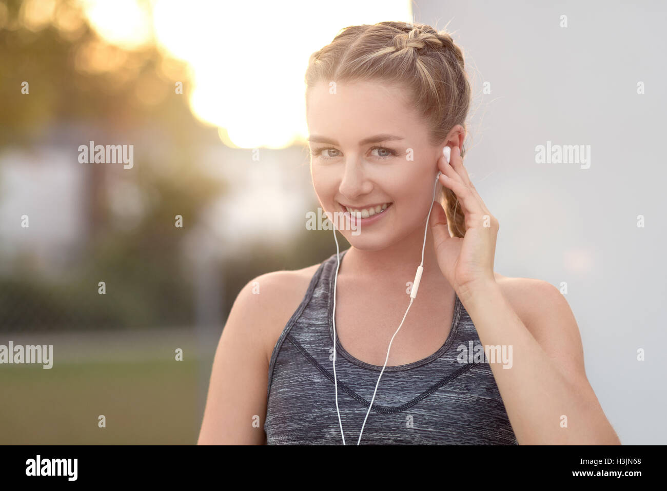 Attraente giovane donna con un bel sorriso ascoltando musica su i tappi per orecchie in una serata estiva con il bagliore del sole di setting Foto Stock