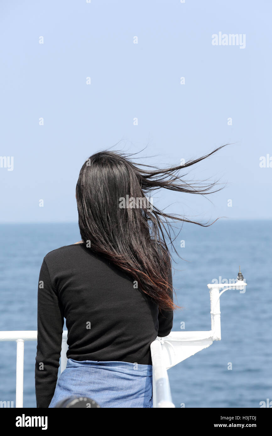 Vista posteriore della giovane donna asiatica con sbandieratori lunghi capelli guardando il mare dal ponte della nave da crociera Foto Stock