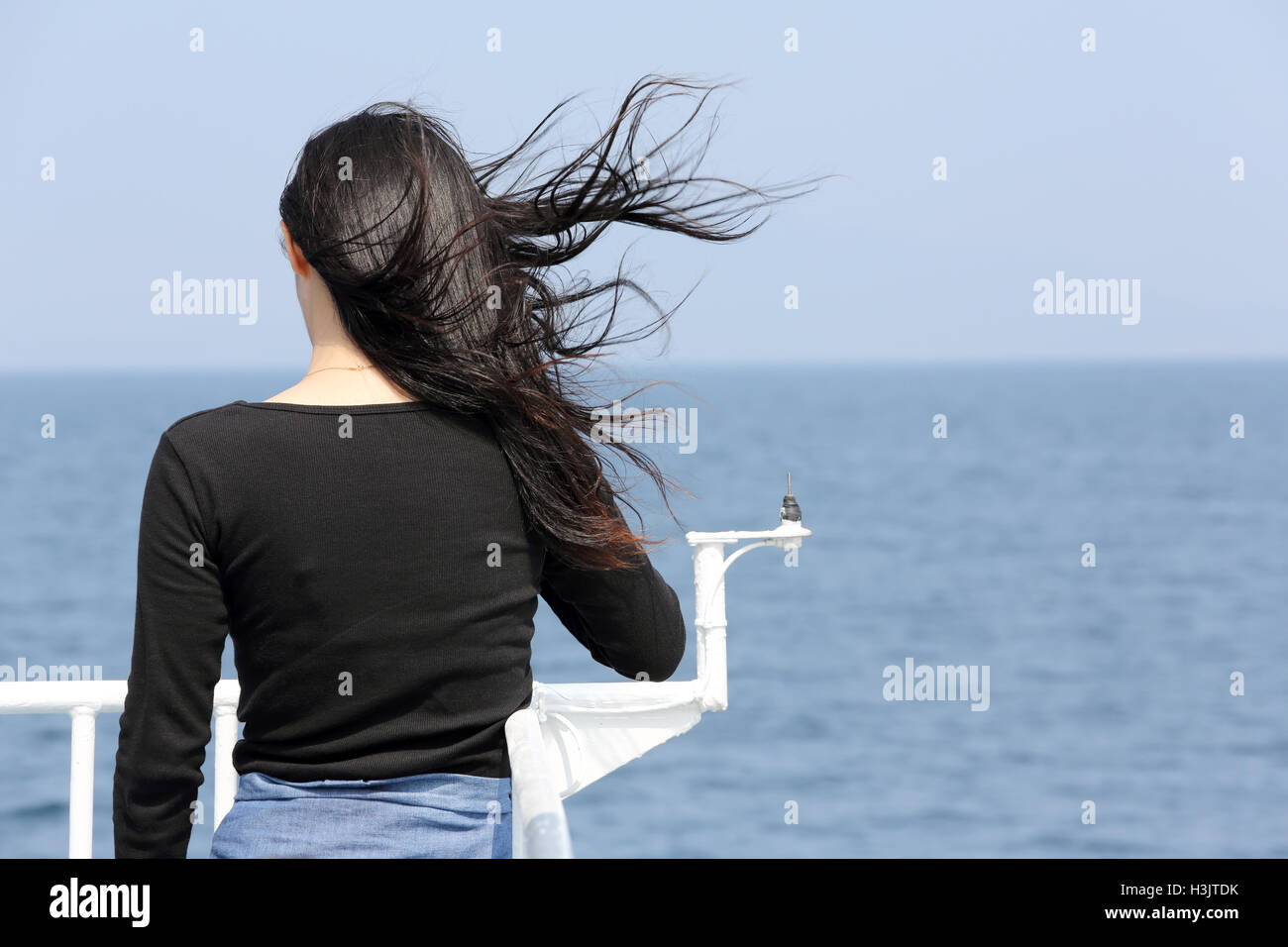 Vista posteriore della giovane donna asiatica con sbandieratori lunghi capelli guardando il mare dal ponte della nave da crociera Foto Stock