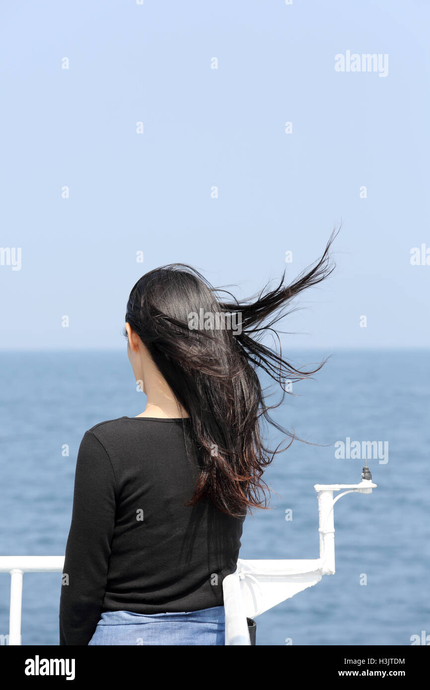 Vista posteriore della giovane donna asiatica con sbandieratori lunghi capelli guardando il mare dal ponte della nave da crociera Foto Stock