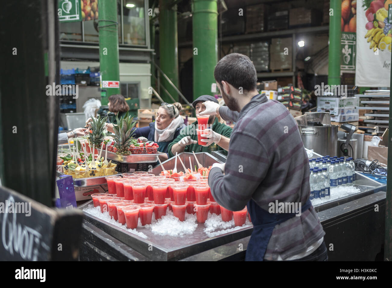 Borough Market, Londra UK Venditore disponendo di succo naturale di frutta in bicchieri di plastica su ghiaccio Foto Stock