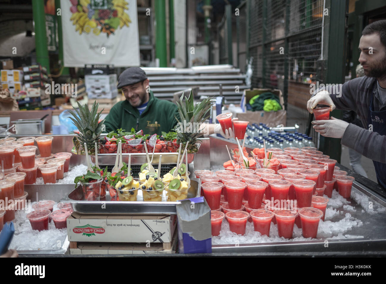 Borough Market, Londra UK Venditore disponendo di succo naturale di frutta in bicchieri di plastica su ghiaccio Foto Stock