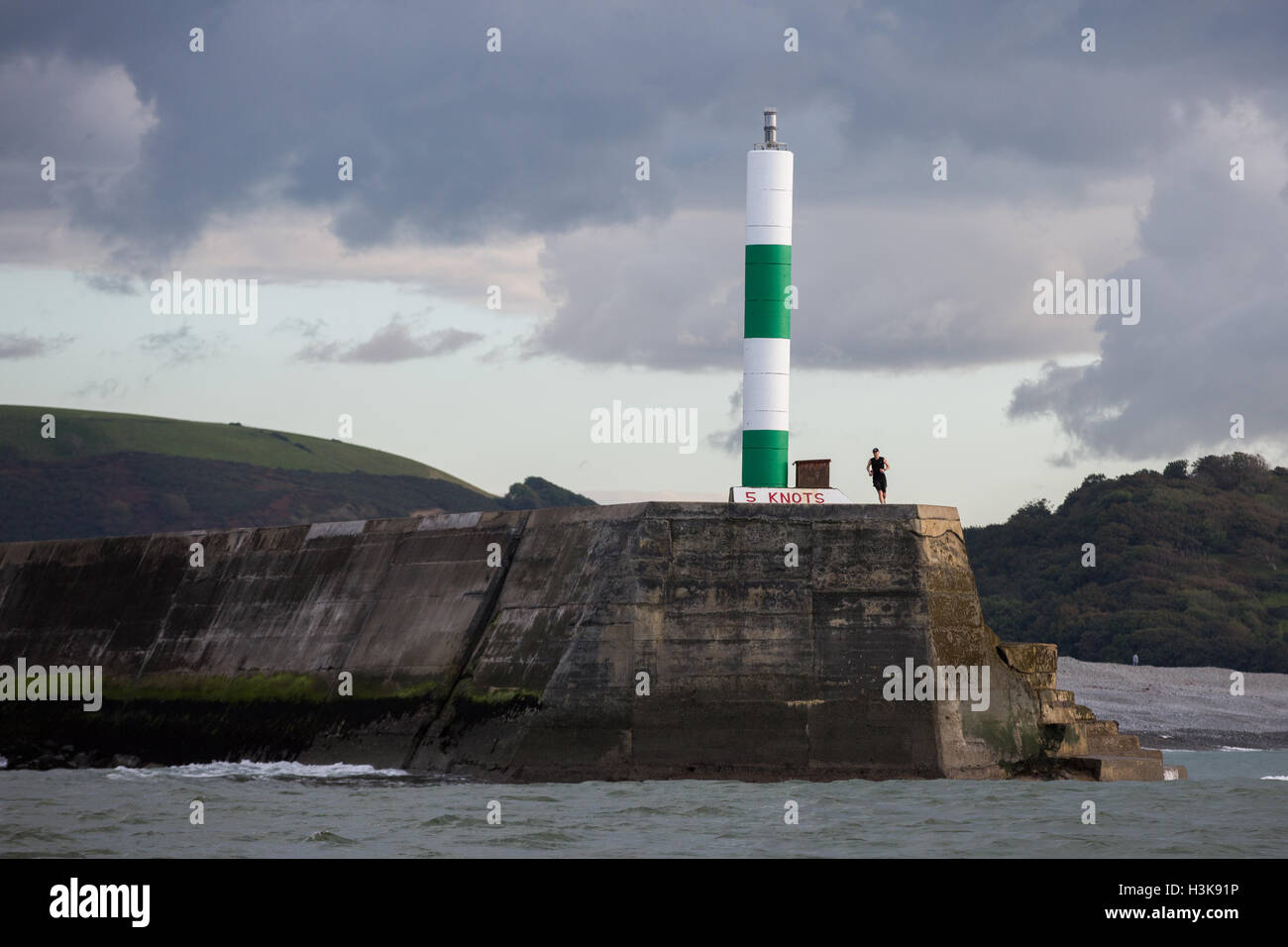 Una persona jogging attorno al marcatore di luce in entrata a Aberystwyth Harbour Foto Stock