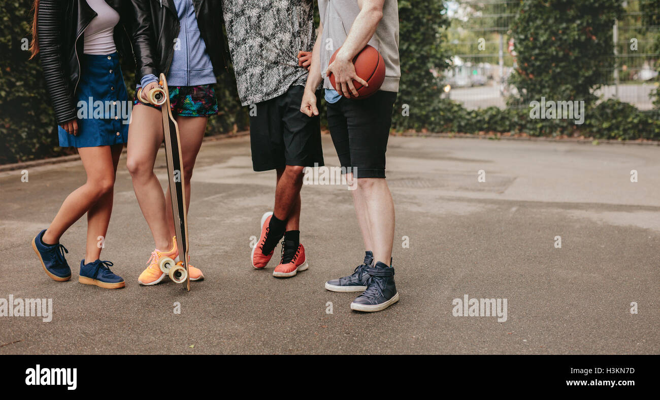 Tagliate il colpo di un gruppo di persone in piedi insieme con la pallacanestro e skateboard. Bassa angolazione con focus su uomini e donne gamba Foto Stock