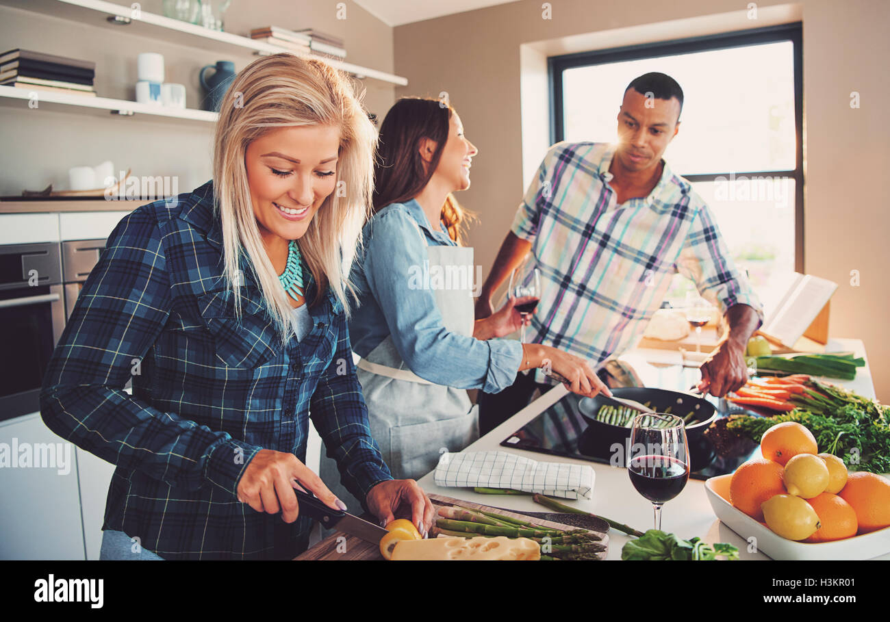 Donna sorridente per affettare ingredienti per pasto con diversi amici di cottura i germogli di asparagi in padella. Foto Stock