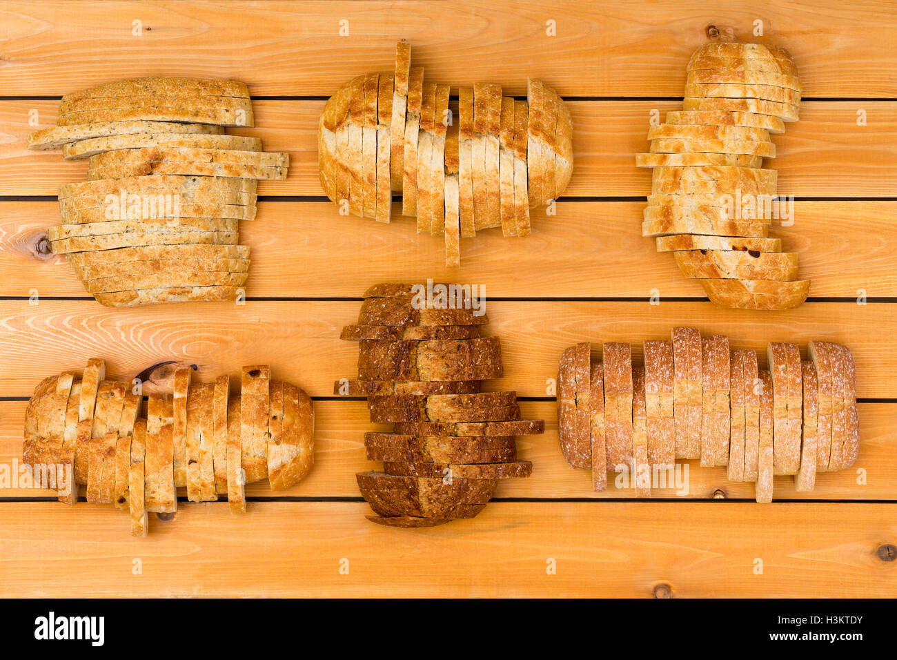 Vista dall'alto in basso su sei fette di pani di varie grano e farina bianca pane in formazione sfalsata su sfondo di legno Foto Stock