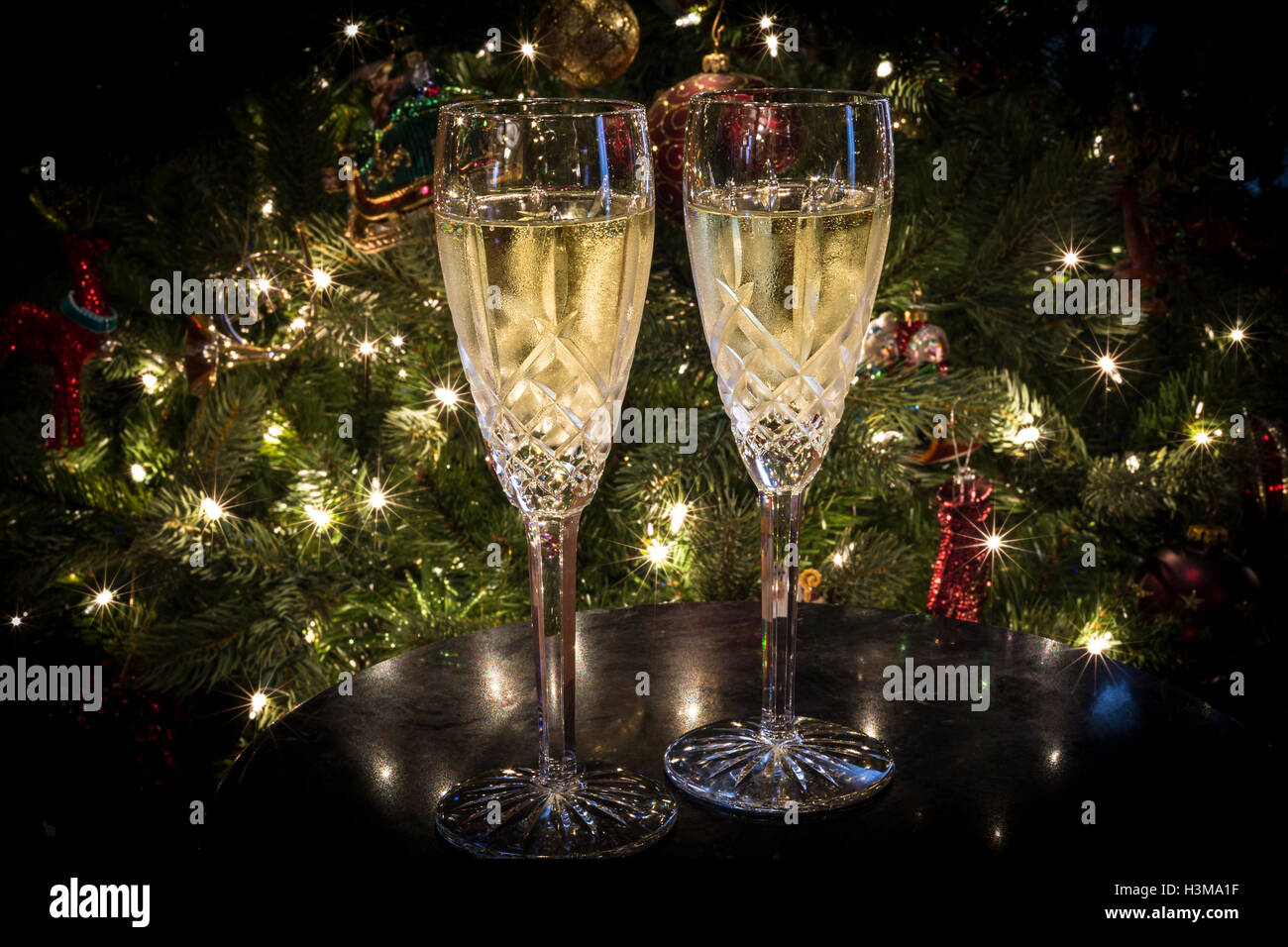 Un set di due flauti champagne riempito con champagne in appoggio su un tavolo di fronte a un albero di Natale. Foto Stock
