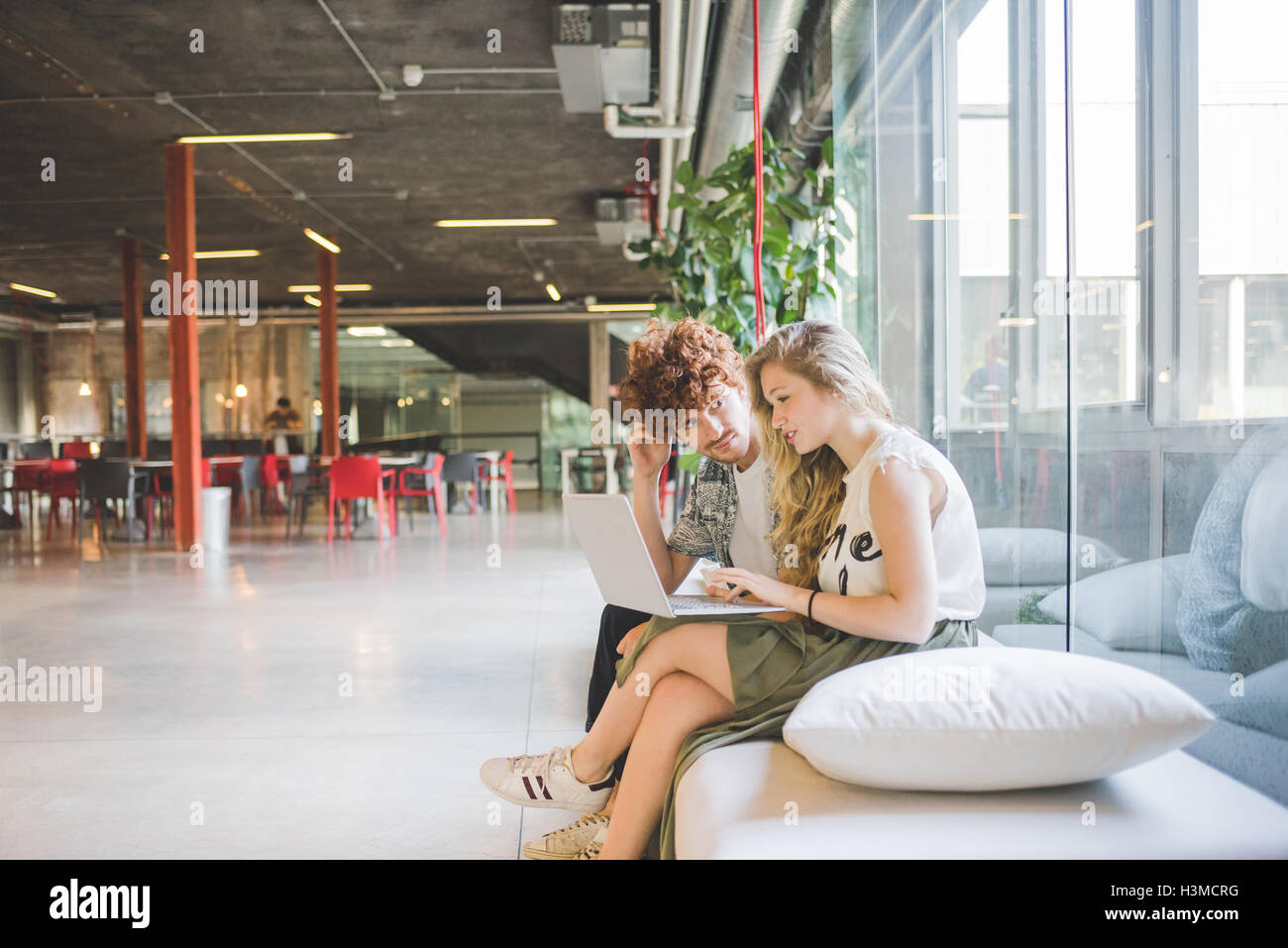 Co-lavoratori che operano sul computer portatile sul divano dalla finestra Foto Stock