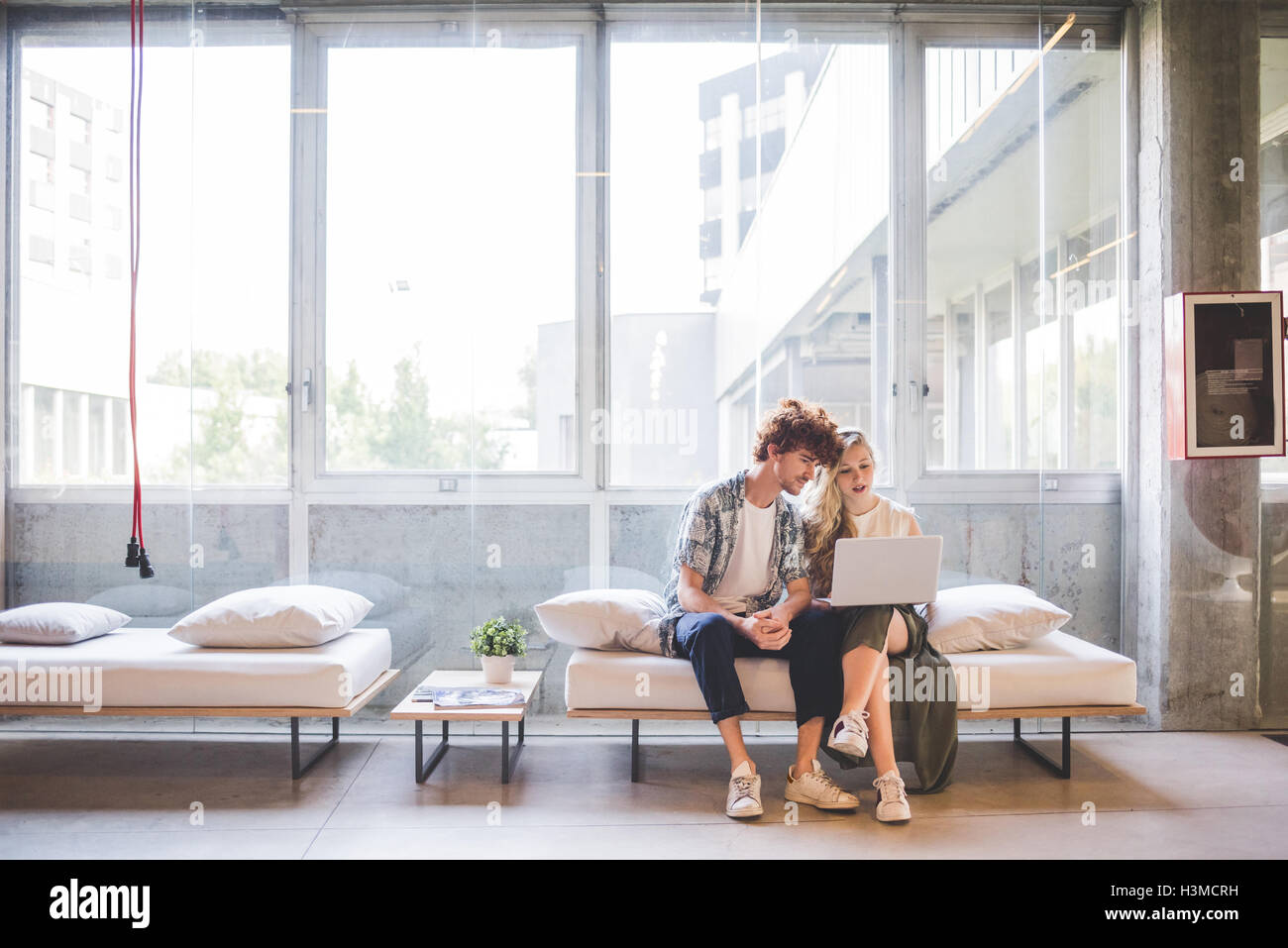 Co-lavoratori che operano sul computer portatile sul divano dalla finestra Foto Stock